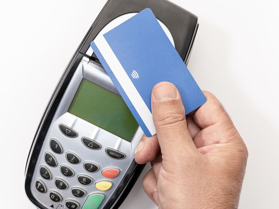 A hand tapping a debit card on a payment terminal